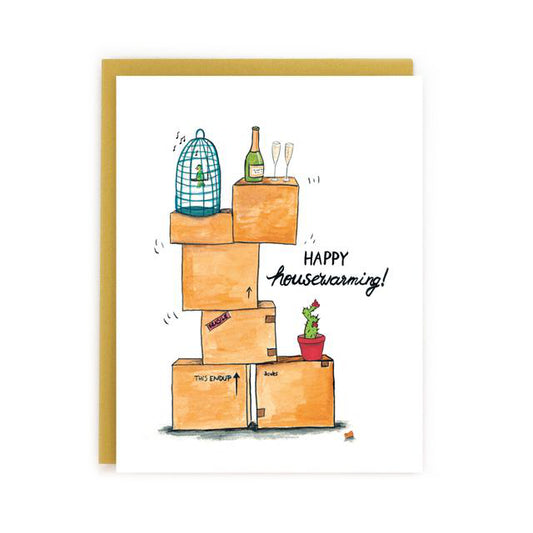 Made in Canada Housewarming greeting card with a drawing of a stack of boxes, a bird cage, a cactus and a bottle of champagne with two glasses. Caption reads: Happy Housewarming!