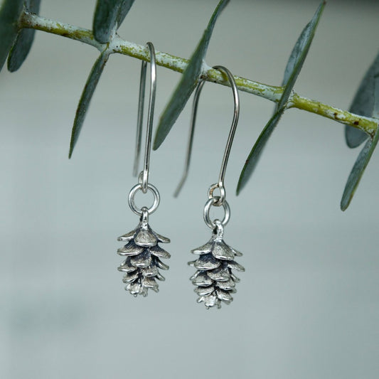 Made in Canada Justine Brooks silver pinecone drop earrings hanging on a fresh green eucalyptus sprig.