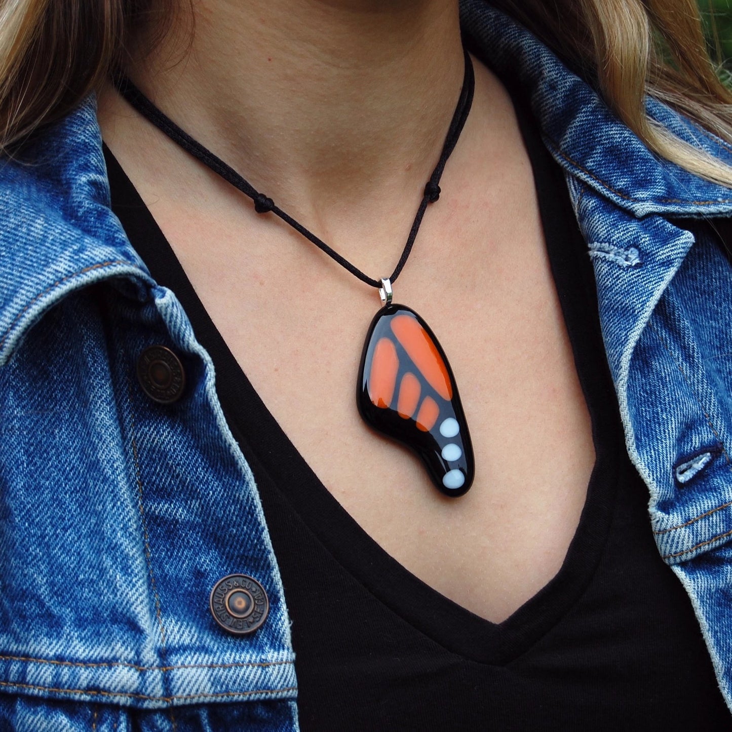 Blonde haired woman wearing a Made in Canada monarch butterfly necklace with a black tee shirt and jean jacket.